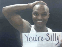 a man is smiling and holding a sign that says you 're silly