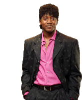 a man in a black suit and pink shirt stands with his hands in his pockets