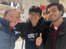 three people posing for a picture with one wearing a george 's college sweatshirt