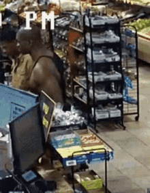 a man in a tank top is standing in front of a computer in a grocery store with a sign that says pm