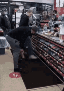 a man is kneeling down in front of a counter in a store while another man stands behind him .