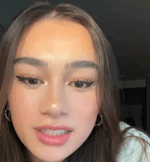 a close up of a woman 's face with a white shirt on and hoop earrings .