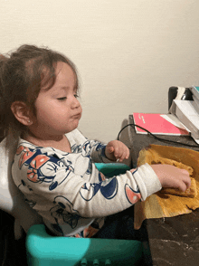 a little girl wearing a minnie mouse shirt is sitting in a high chair eating food