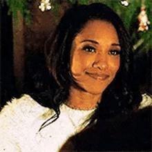 a woman is smiling in front of a christmas tree and looking at the camera .