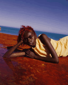 a woman with red hair is laying on a red surface in front of the ocean