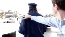 a man is putting his hand on a woman 's shoulder while she is wearing a graduation cap and gown .