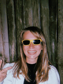 a woman wearing yellow sunglasses is smiling and pointing