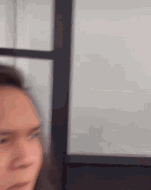 a man with long hair is making a funny face while standing in front of a window .