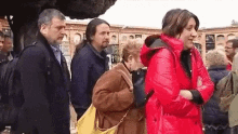 a group of people are standing in a cemetery . one of the people is wearing a red jacket .