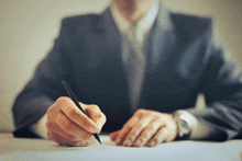 a man in a suit writes on a piece of paper with a pen