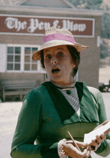 a woman in a green dress stands in front of a building that says the pen & blow