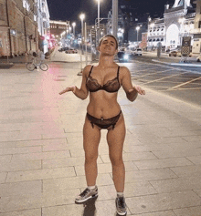 a woman in lingerie and sneakers stands on a sidewalk at night