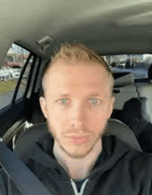 a man with a beard is sitting in the back seat of a car and looking at the camera .