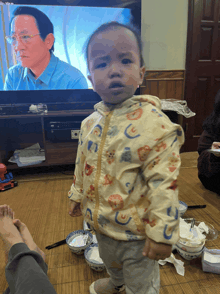 a baby is standing in front of a tv screen that shows a man with glasses