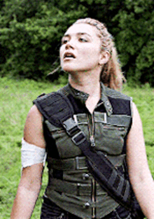 a woman is standing in a field wearing a vest and a bandage on her arm .