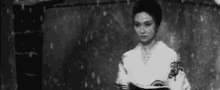 a black and white photo of a woman in a kimono holding a book in the rain .