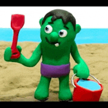 a green cartoon character is holding a shovel and a bucket on the beach .