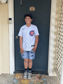 a young boy wearing a cubs jersey stands in front of a blue door