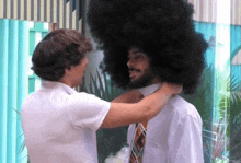 a man with a huge afro is getting his tie adjusted by another man