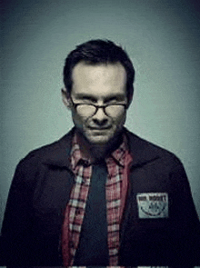 a man wearing glasses , a plaid shirt , and a black jacket is smiling .