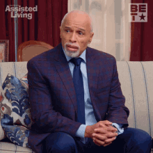 a man in a suit and tie is sitting on a couch with the assisted living logo in the background