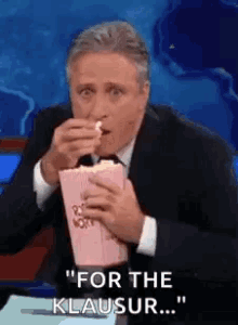 a man in a suit is eating popcorn while saying " for the klausur "