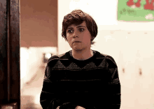 a young man in a black sweater is standing in a hallway with his arms crossed and looking at the camera .