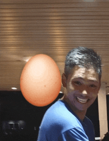 a man in a blue shirt smiles in front of a large orange balloon