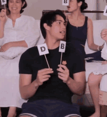 a man in a black shirt is sitting on a couch holding a sign with the letter d and b on it .