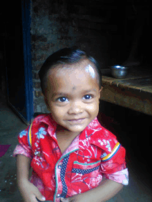 a young boy wearing a red shirt with flowers on it