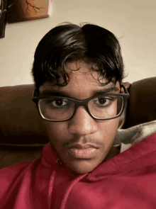 a young man wearing glasses and a red shirt looks at the camera