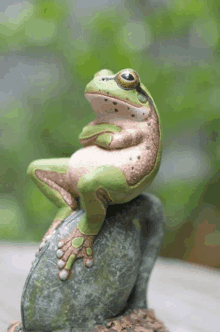 a frog statue sits on a rock with its arms crossed