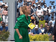 a woman in a green dress stands in front of a crowd of people and holds a piece of paper that says por 10