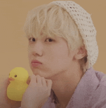 a young man wearing a knitted hat is holding a yellow rubber duck in his hand