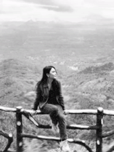 a woman sits on a wooden railing overlooking a valley