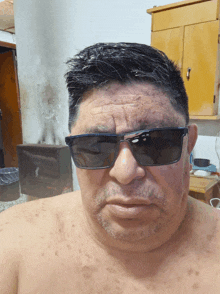 a shirtless man wears sunglasses and looks at the camera