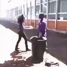 a woman is standing next to a trash can and a man is standing next to a trash can .