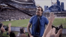 a man in a blue shirt and tie is standing in front of a crowd of people at a stadium .