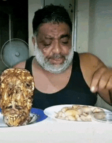 a man with a beard is sitting at a table with plates of food and a lion 's head .