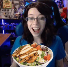 a woman is holding a bowl of salad with chicken breasts and tomatoes