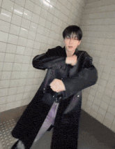 a man in a black coat is dancing in front of a white tile wall