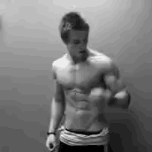 a shirtless man is flexing his muscles in front of a wall in a black and white photo .