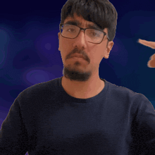 a man with glasses and a beard is pointing his finger at his mouth