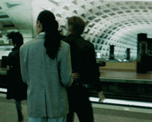 a man and a woman are standing on a subway platform looking at a sign that says ' subway ' on it