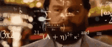 a man with a beard is standing in front of a screen with mathematical equations written on it .