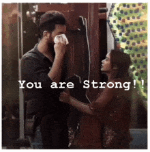 a man wipes his face with a napkin while a woman looks on with the words " you are strong " below him