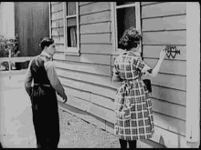 a man and a woman are standing in front of a house and the woman is writing on the side of the house .