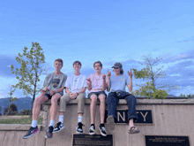 a group of young men sit on a wall with a plaque that says ' n.y. ' on it