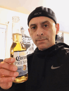 a man wearing an xbox hat holds up a bottle of corona