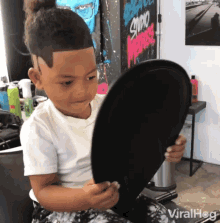 a young boy is looking at himself in a mirror with a sign that says studio on the wall behind him